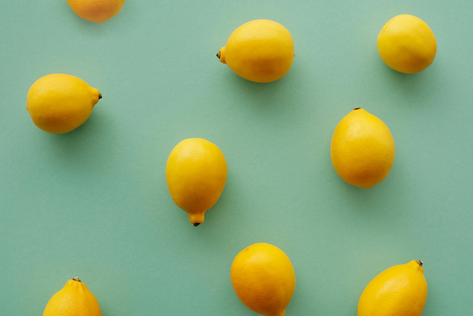 Vibrant yellow lemons arranged on a pastel green background, creating a fresh and vibrant flat lay composition.